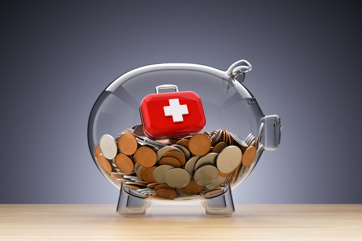 Glass piggy bank with red cross symbol, filled with coins.